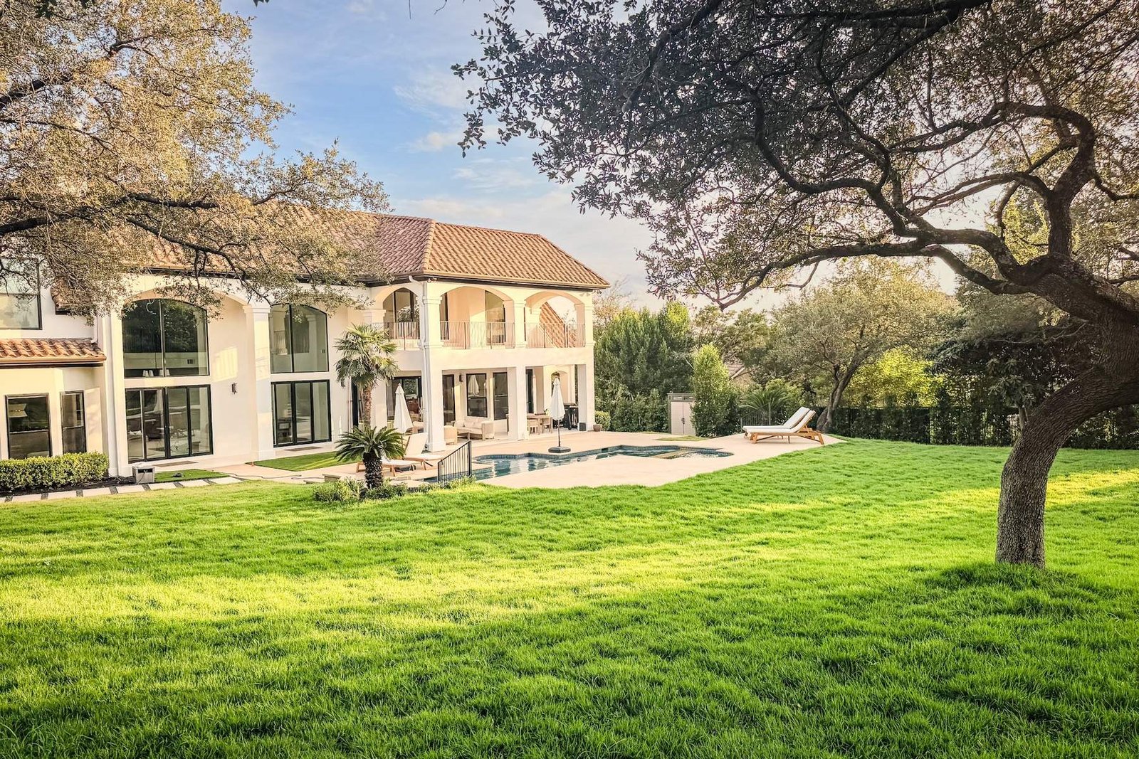 A broad lawn sweeping toward a stucco house and pool beneath a live oak
